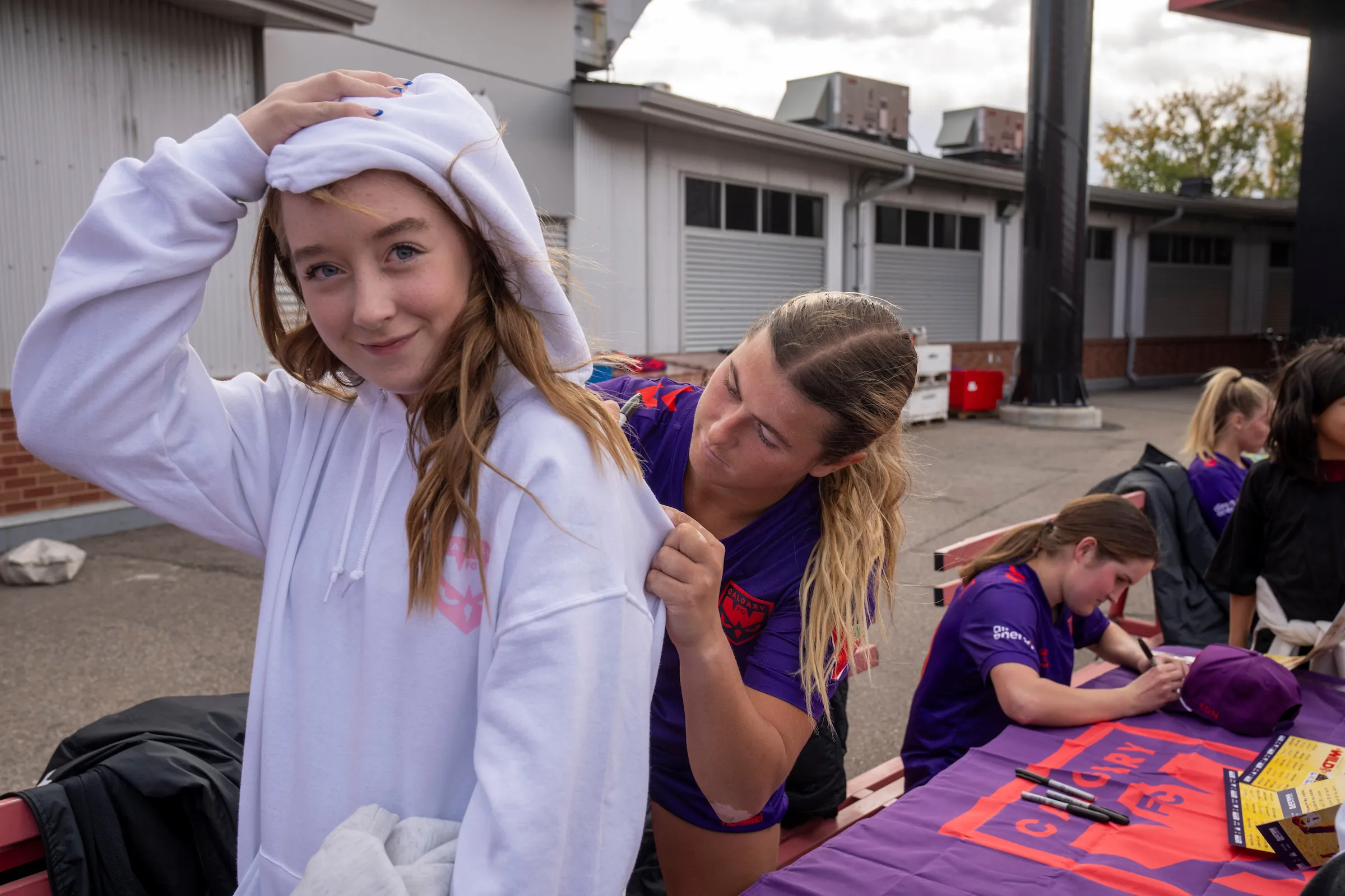 Calgary Wild FC player signing the back of a fan's hoodie at the signing table after a match
